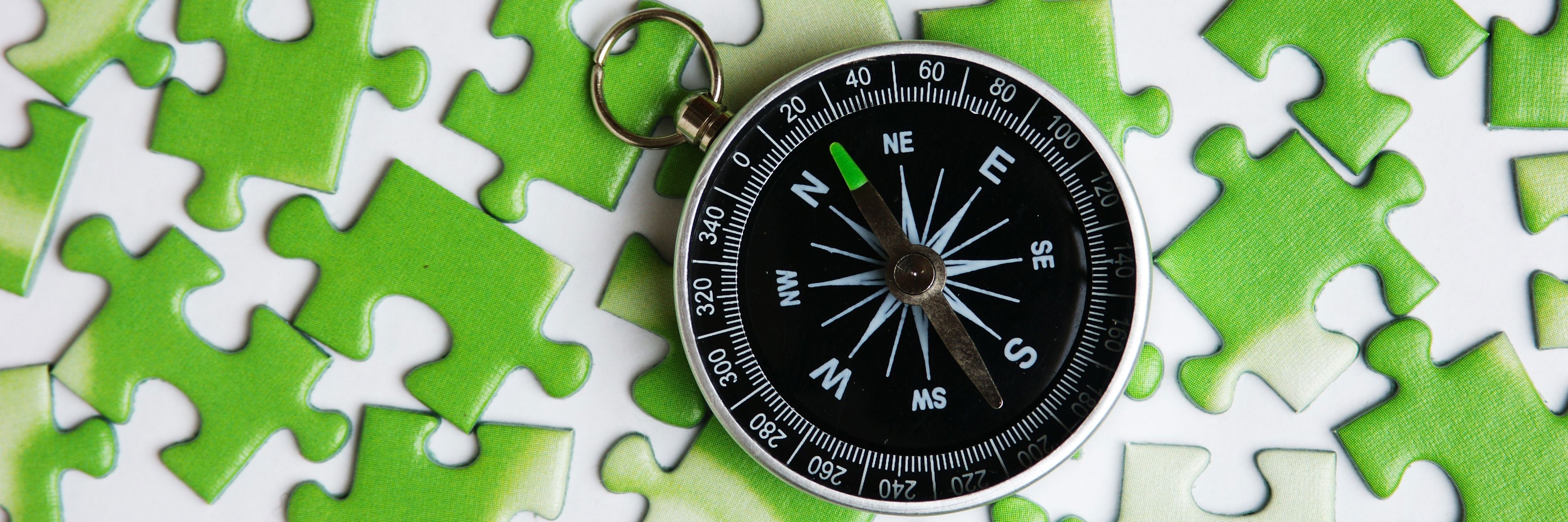 Et kompas der ligger ovenpå grønne puslespilsbrikker