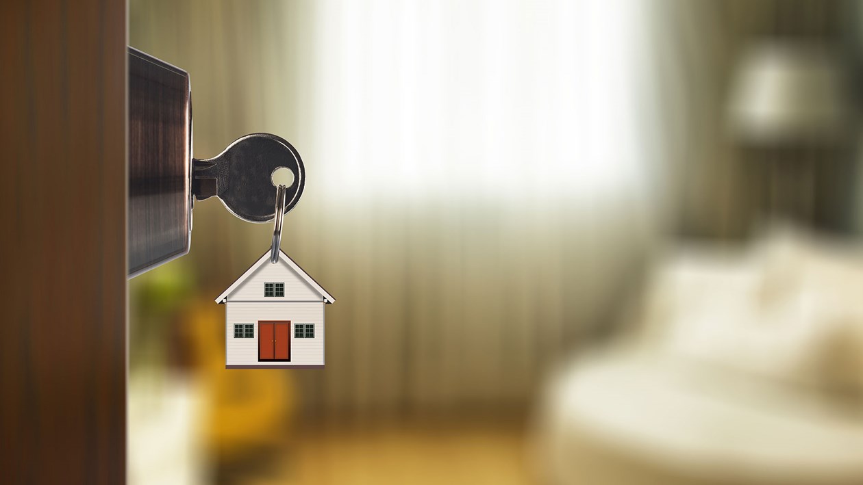 Nøgle i lås med et lille hus som nøglering