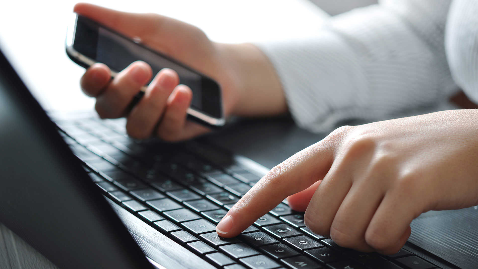 Hænder, tastatur og mobiltelefon