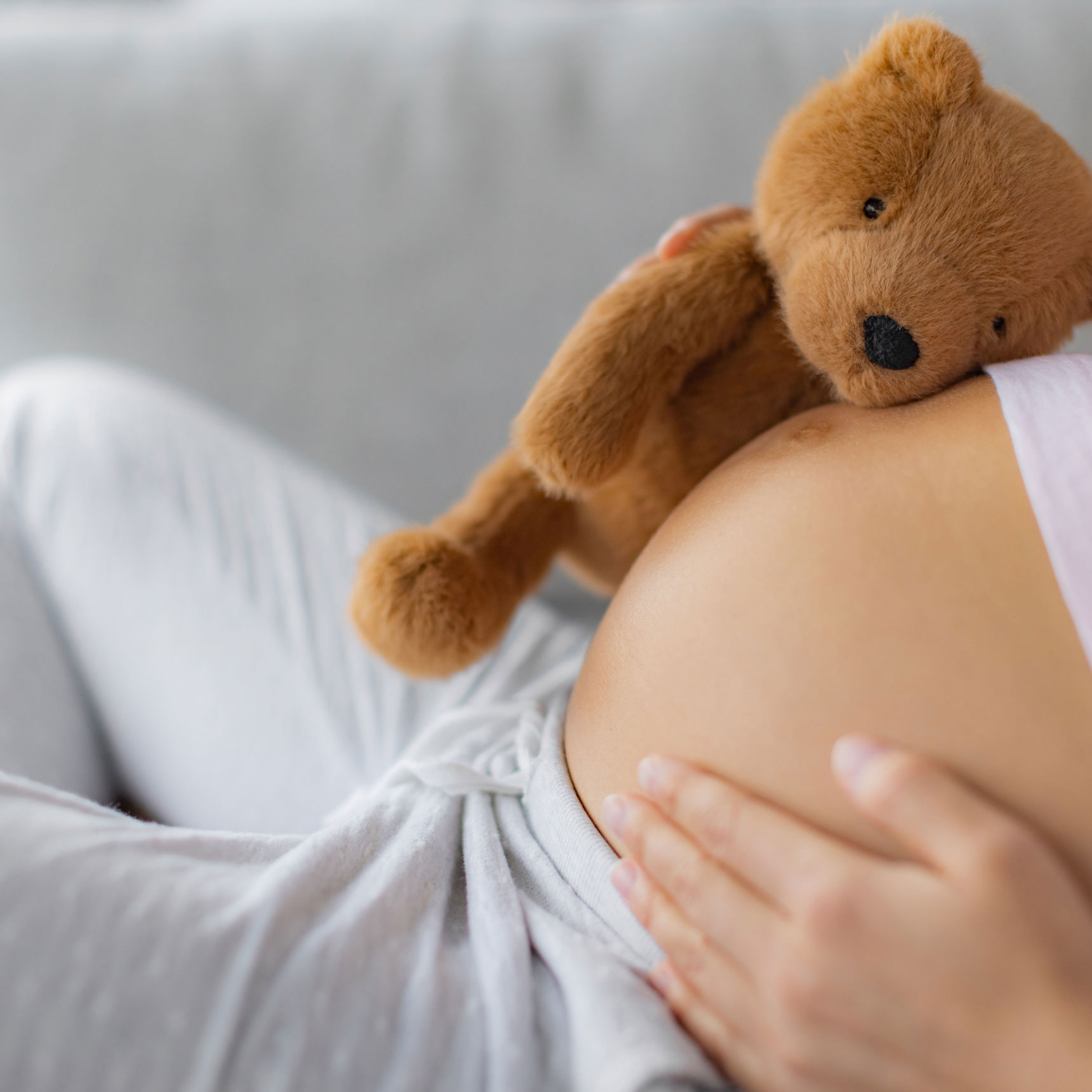 En gravid der ligger med en bamse på maven