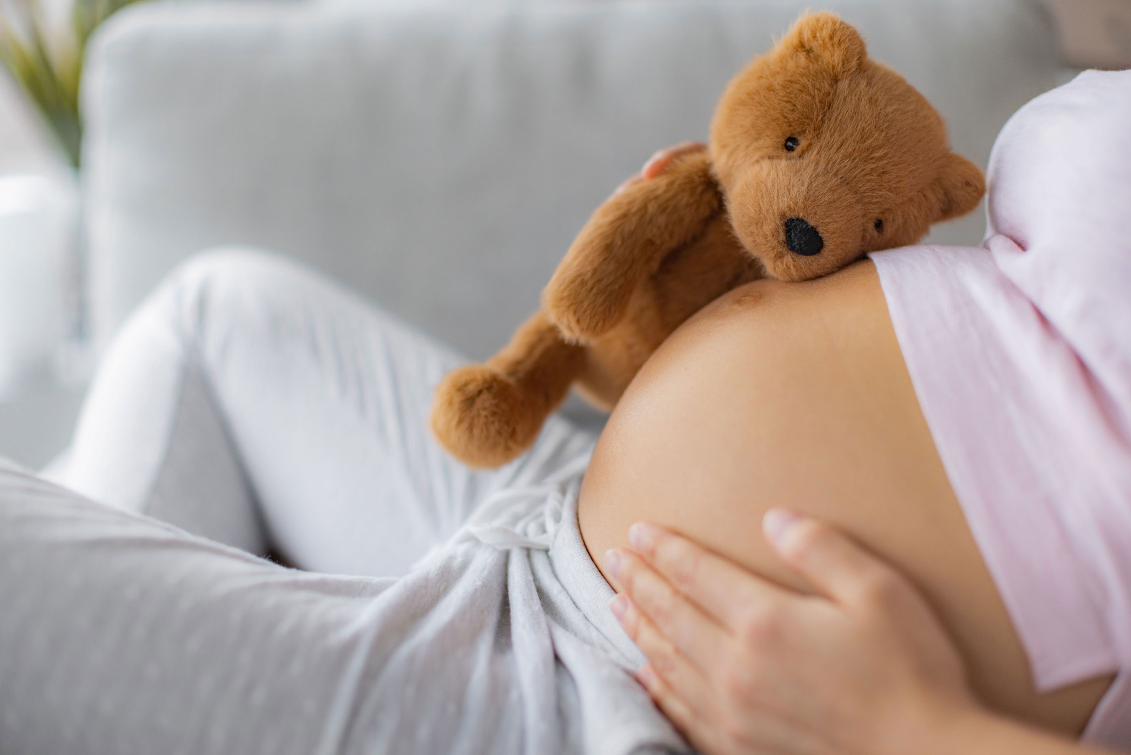 En gravid der ligger med en bamse på maven