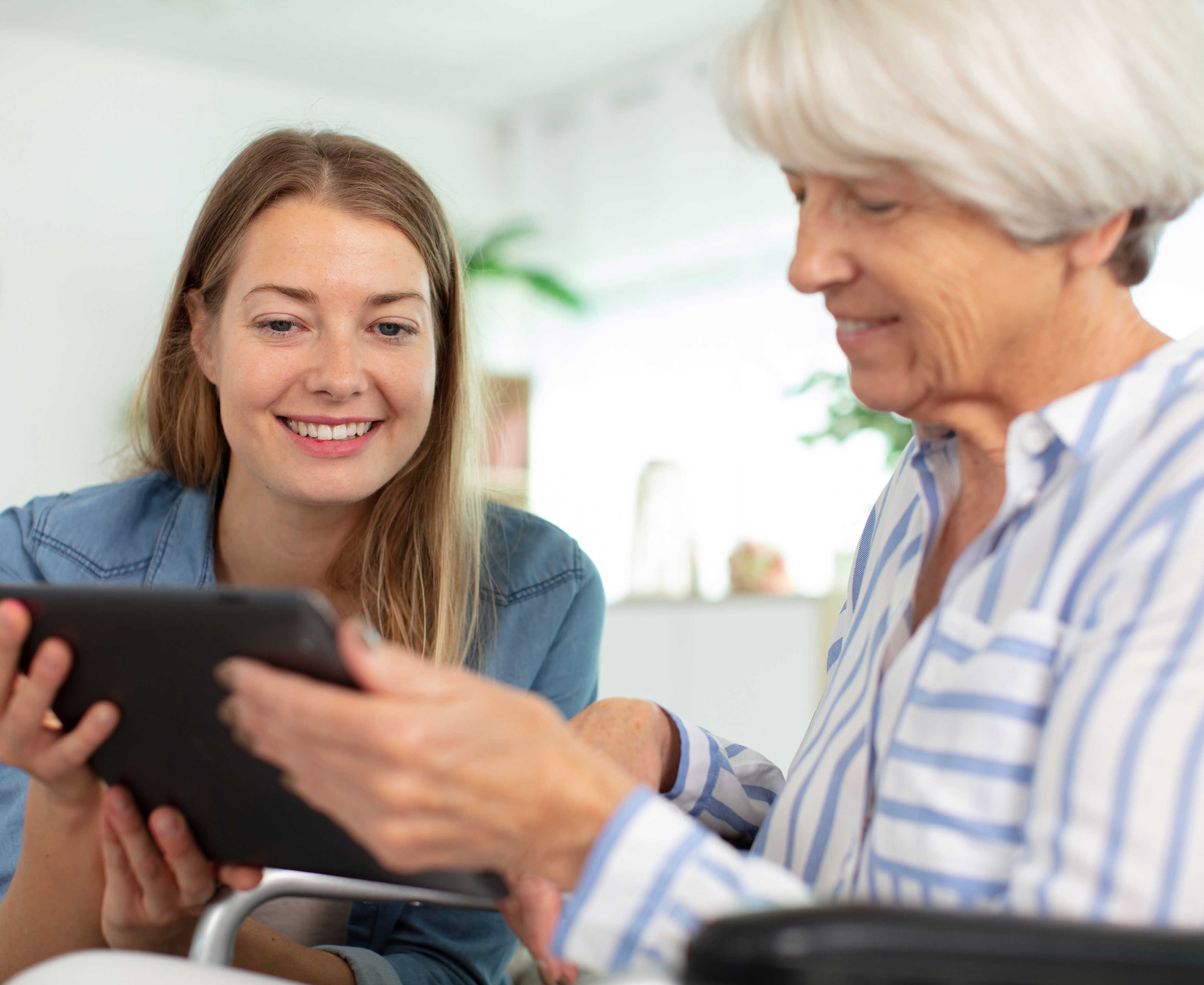 Yngre kvinde der hjælper en ældre kvinde med hendes iPad