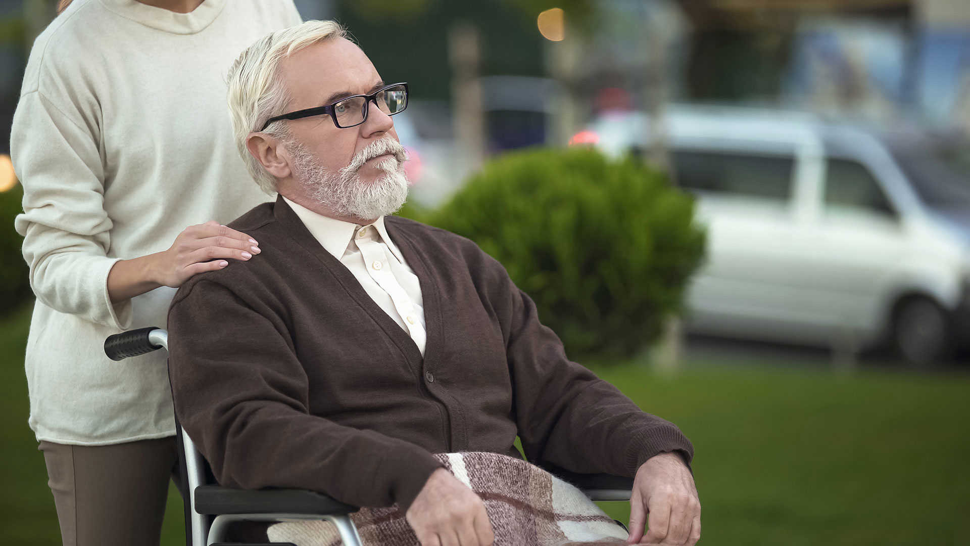 En ældre herre i en kørstol med en kvindes hænder på skulderne