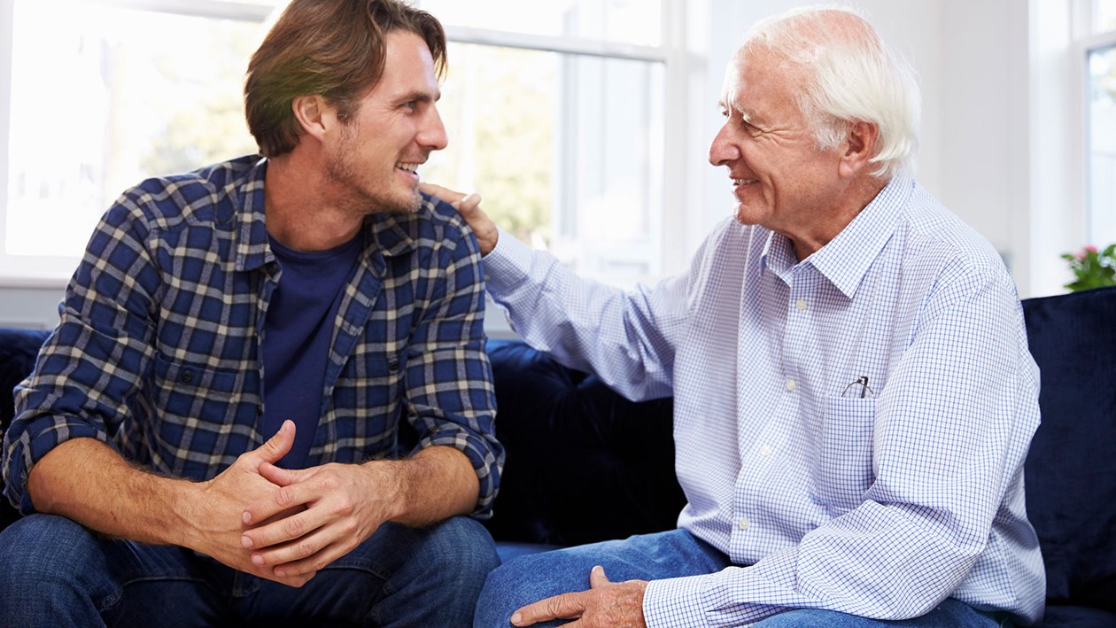 En ældre og en yngre mand der smilende sidder i en sofa