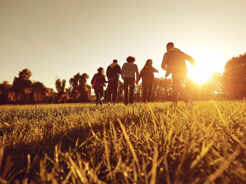 Ryggen af unge der løber på en græsplæne i solnedgangen