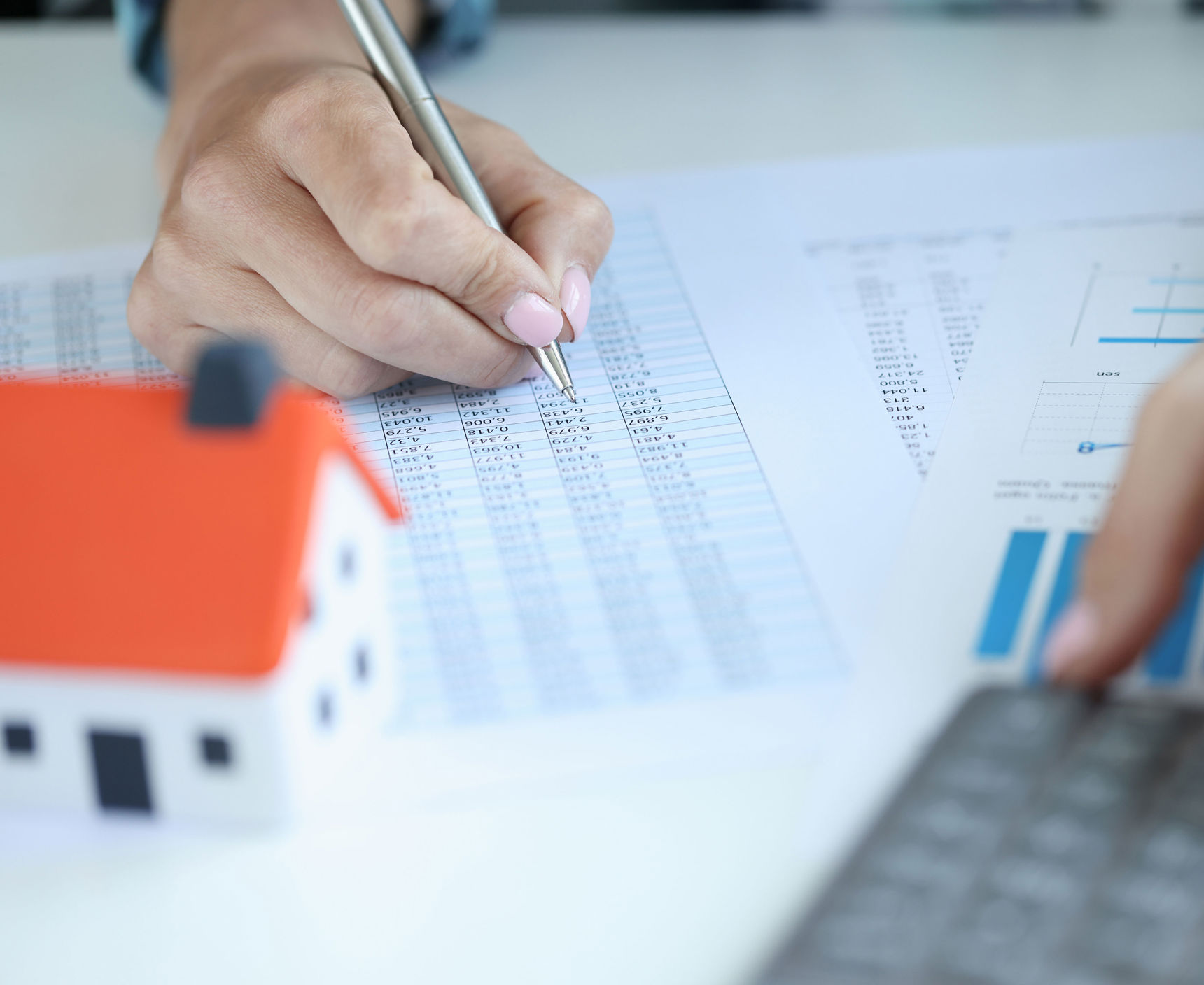 Hånd på et regneark med en lommeregner og et lille bitte hus foran sig