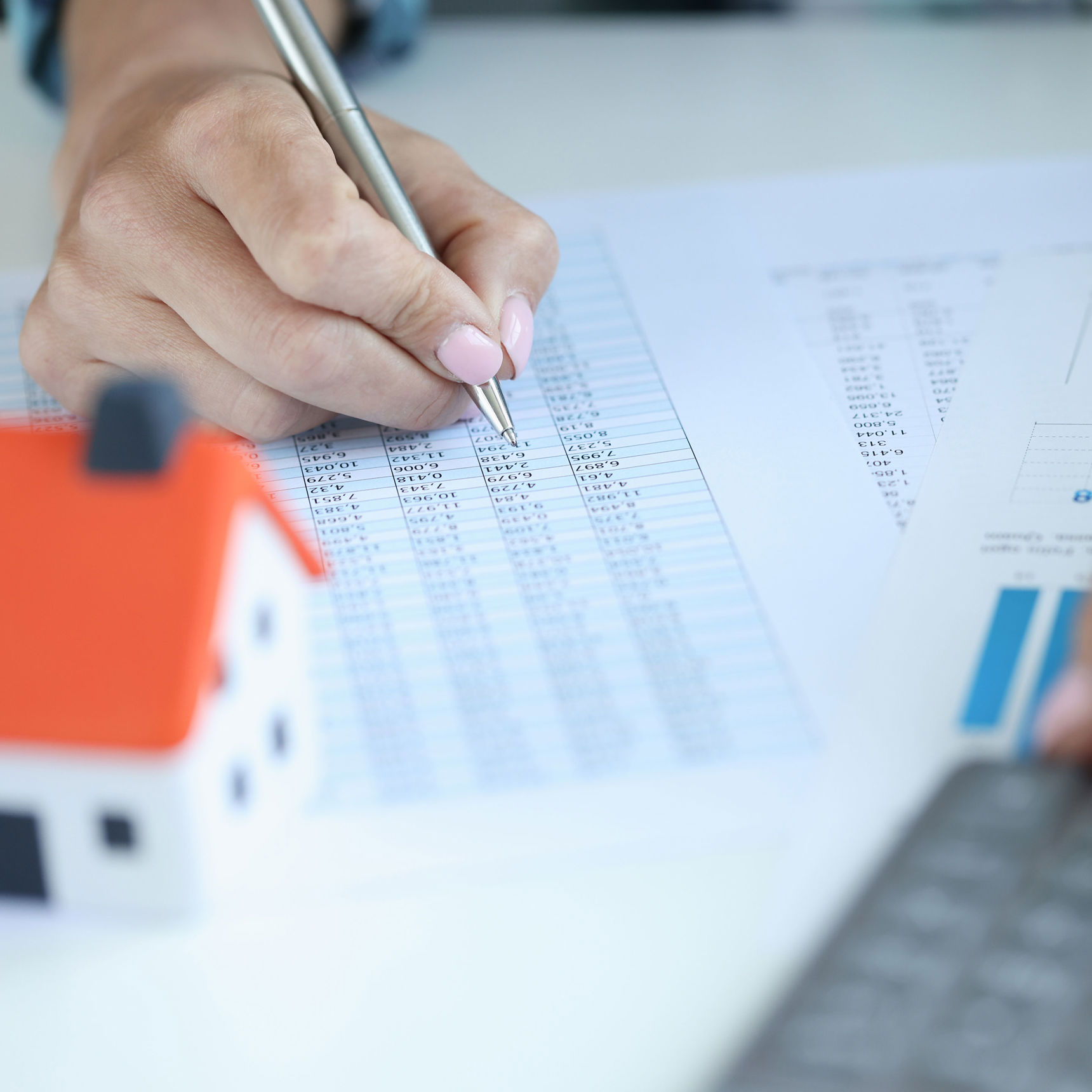 Hånd på et regneark med en lommeregner og et lille bitte hus foran sig