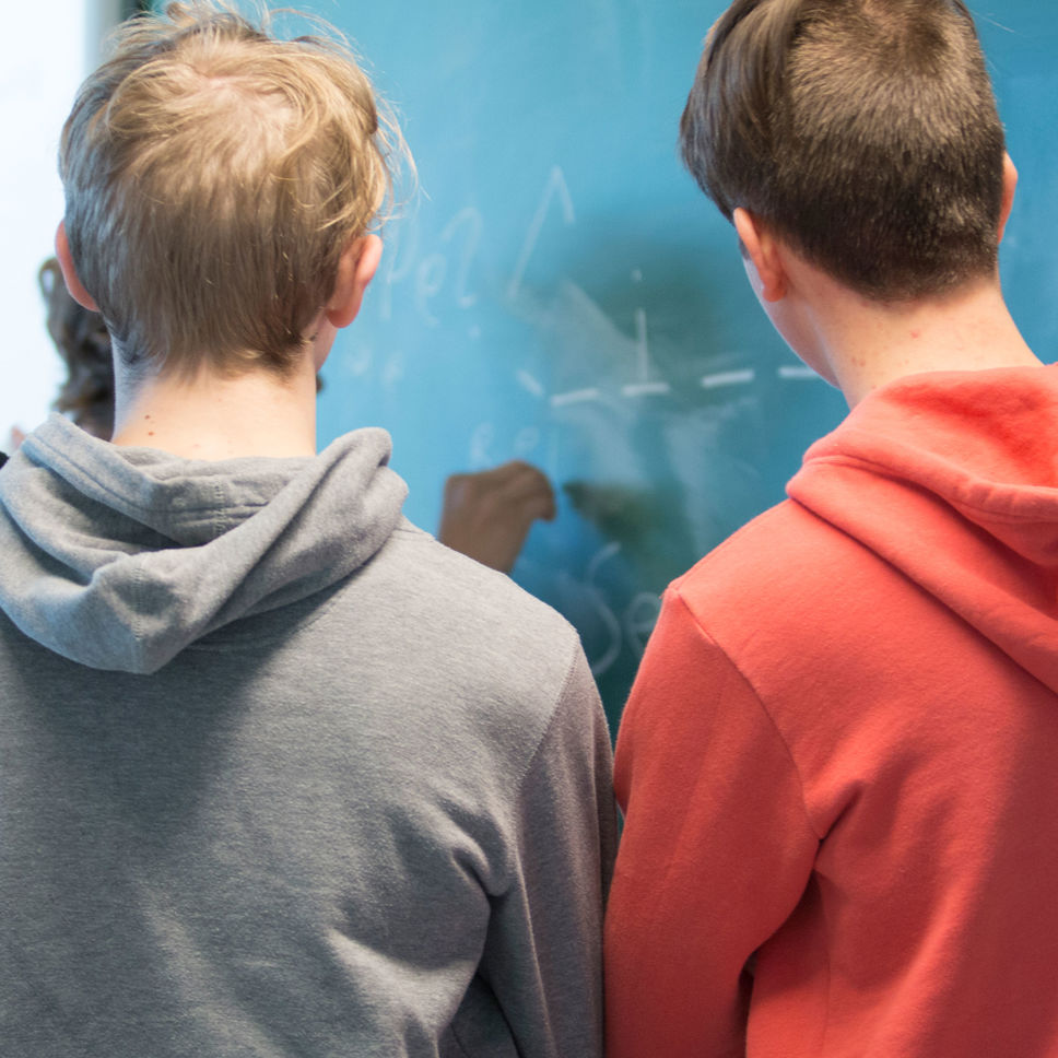 Tre skolelever med ryggen til der skriver på en tavle