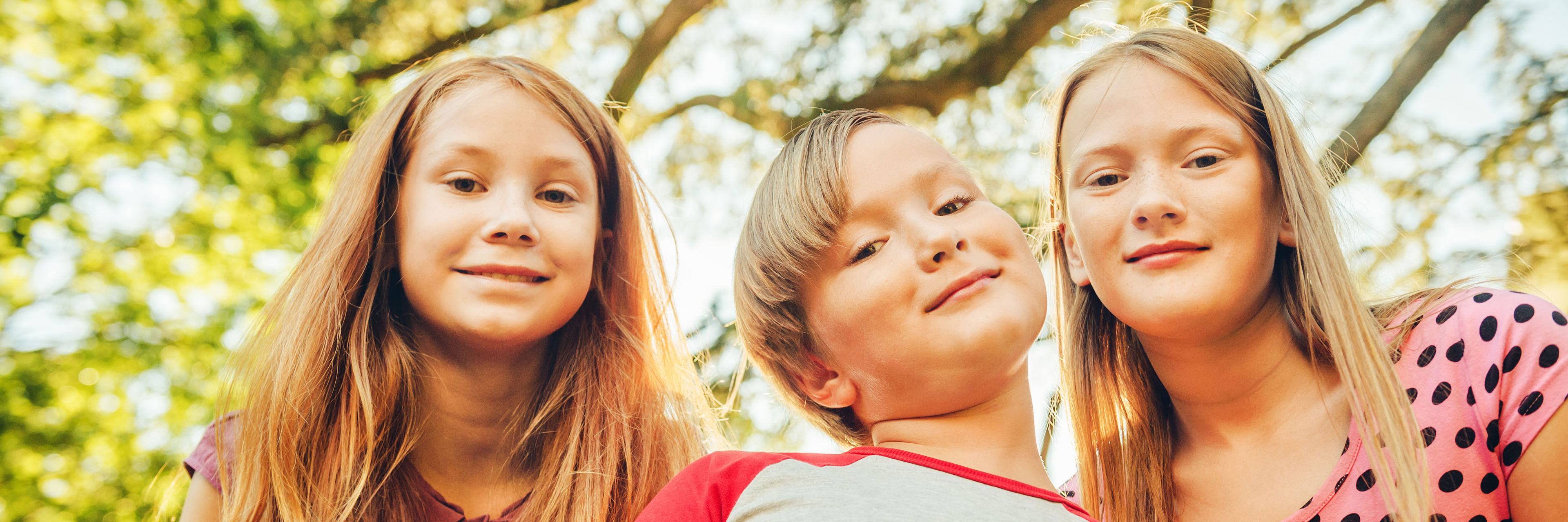 Tre børn med træ og solsikn i baggrunden