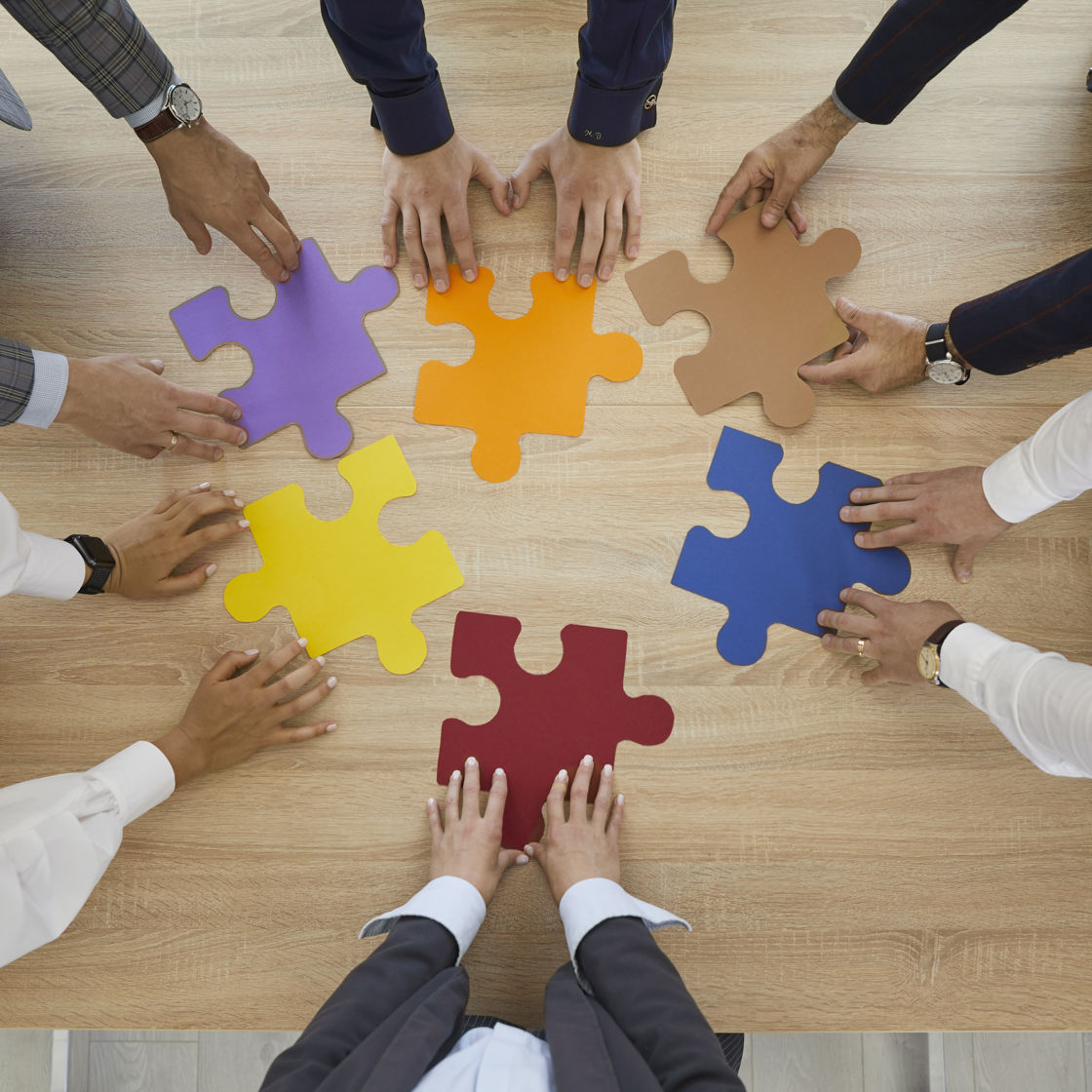 Hænder der hver holder en puslespilsbrik på et bord