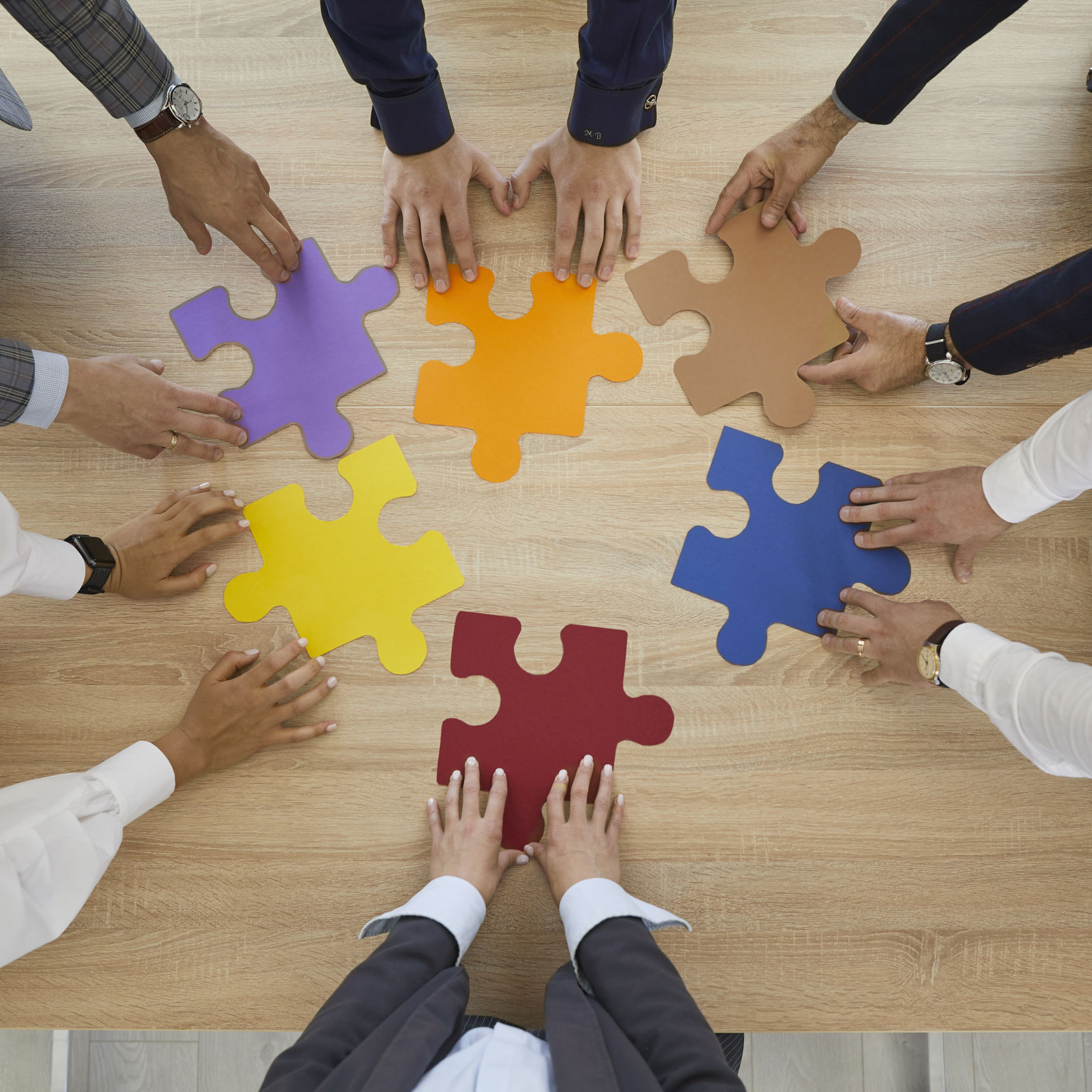 Hænder der hver holder en puslespilsbrik på et bord