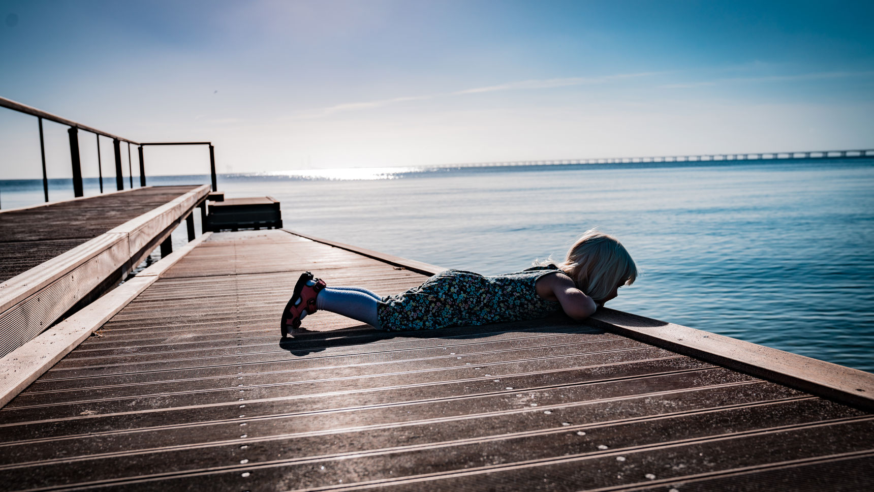 Pige der ligger på maven og kigger på vandet fra en badebro