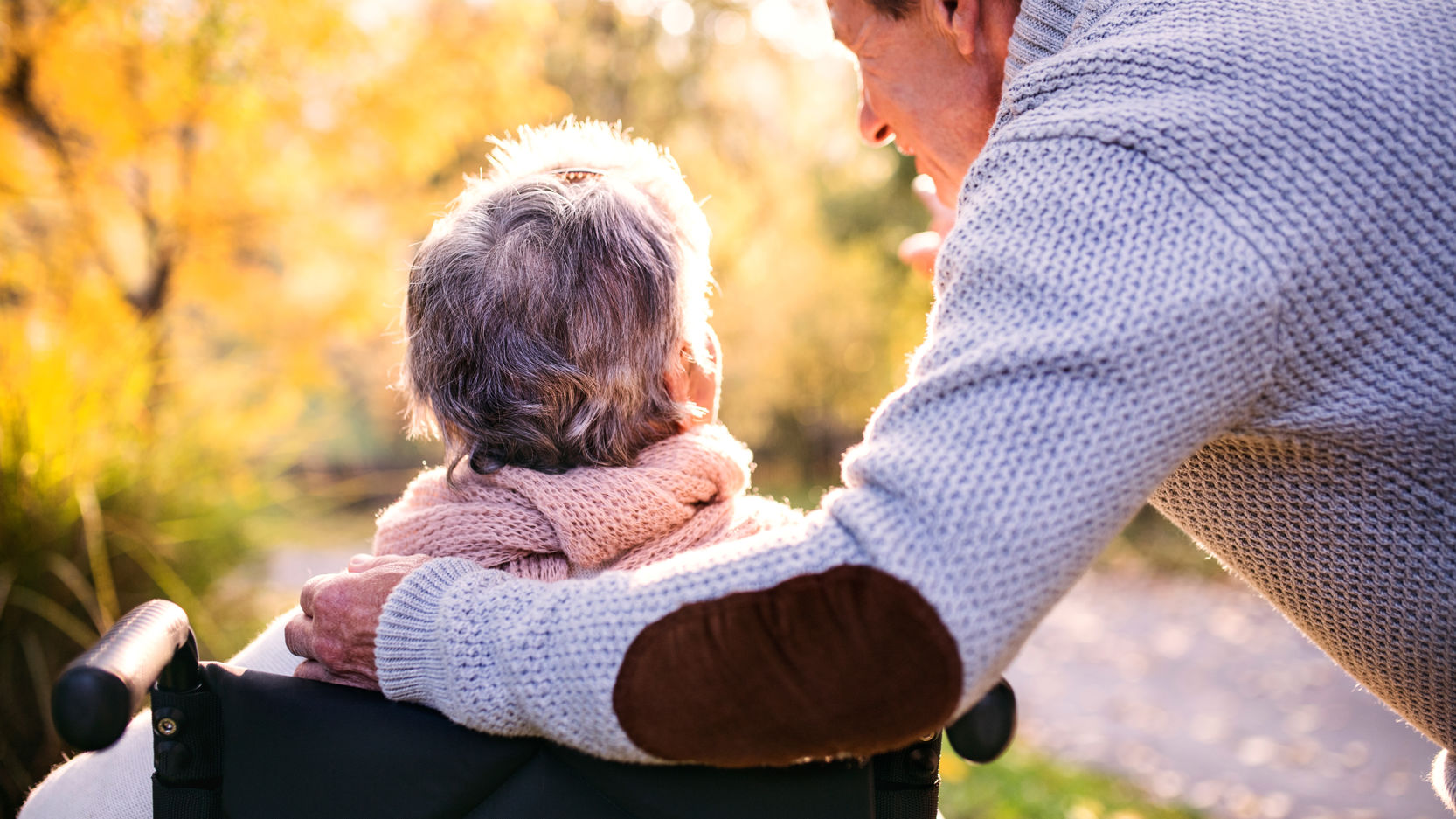 Dame i kørestol hvis mand holder om hende bag fra