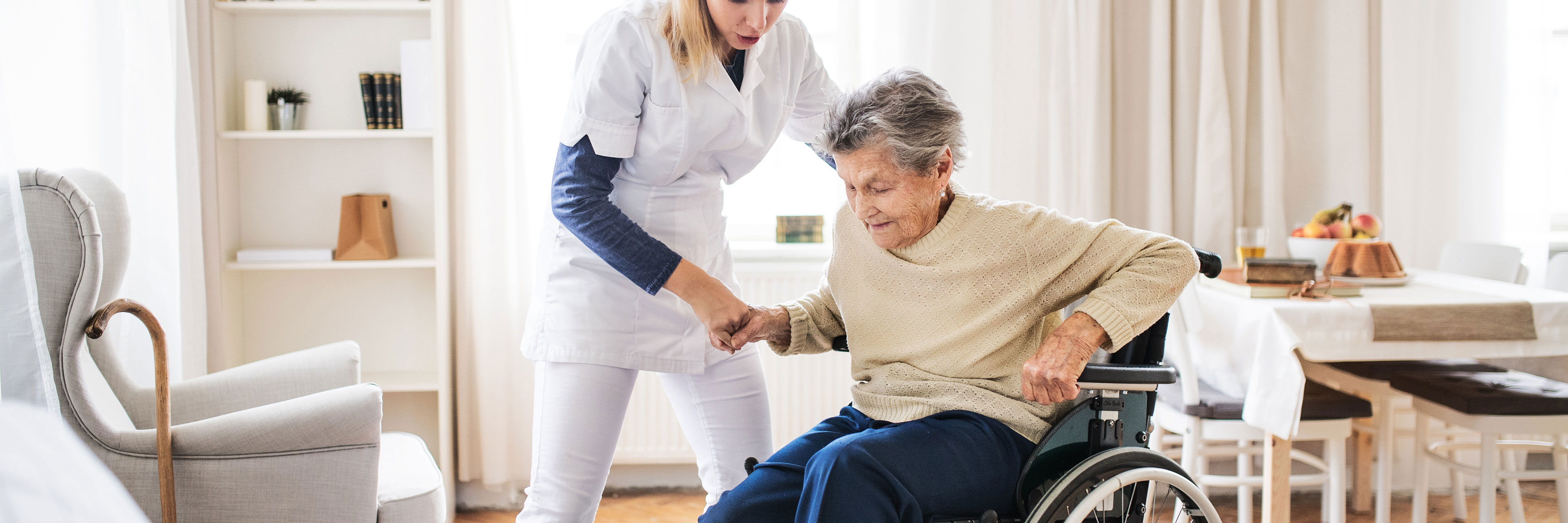 Plejer der hjælper en ældre dame i rullestol