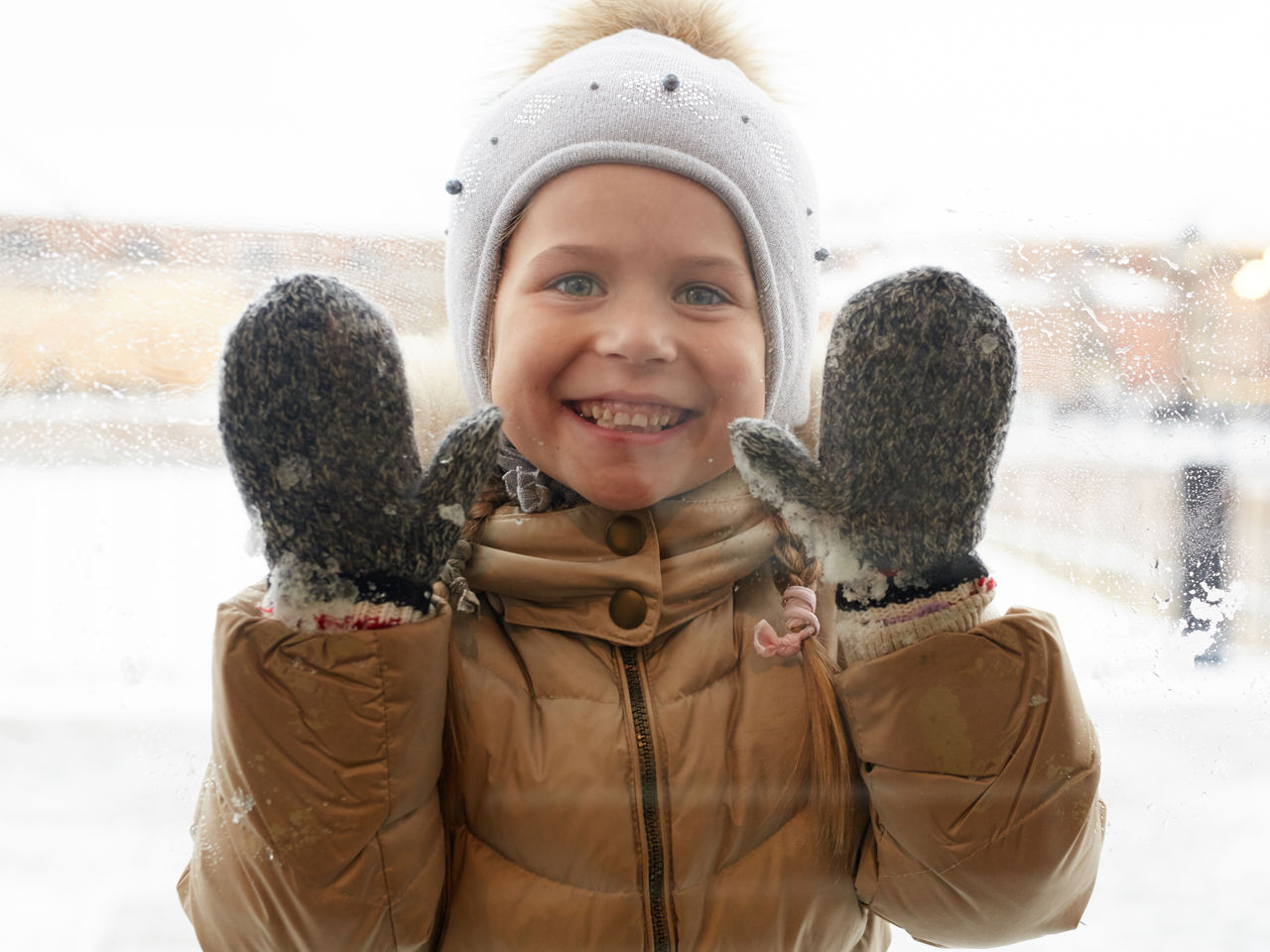 Barn med hue og handsker der kigger gennem en rude