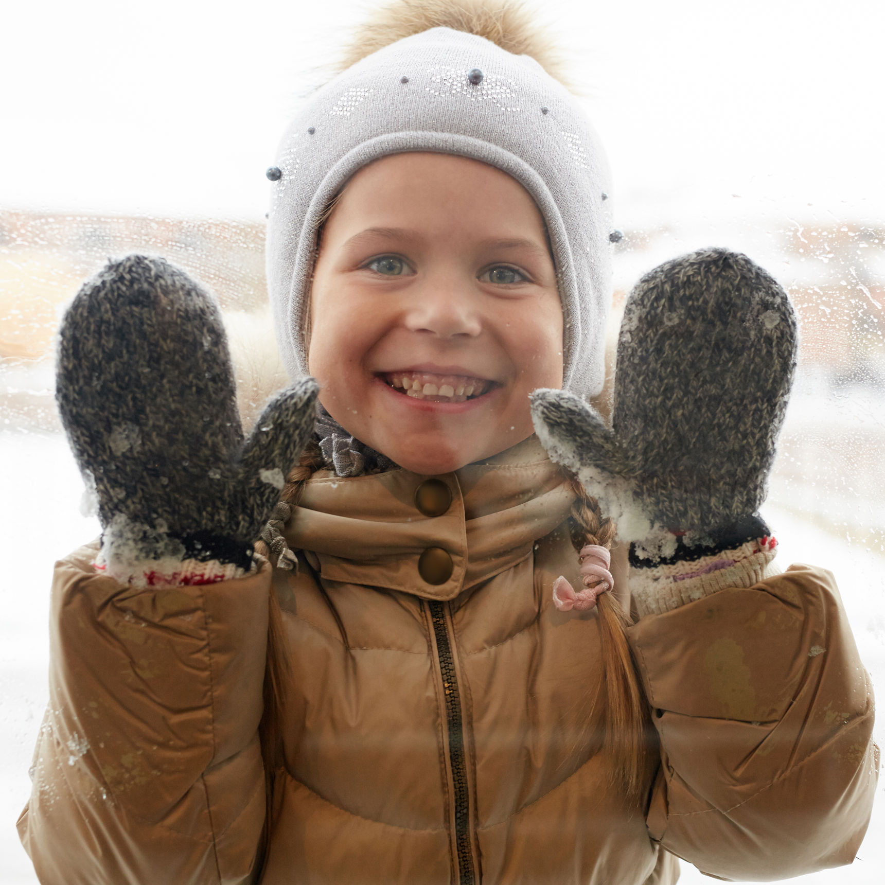 Barn med hue og handsker der kigger gennem en rude