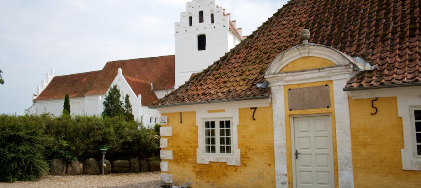 Aunslev Kirke med gul bygning i forgrunden